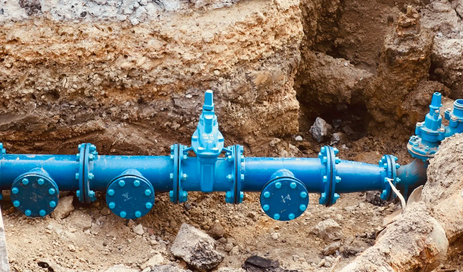 Exposed underground water pipe and valves revealed in an open excavation trench